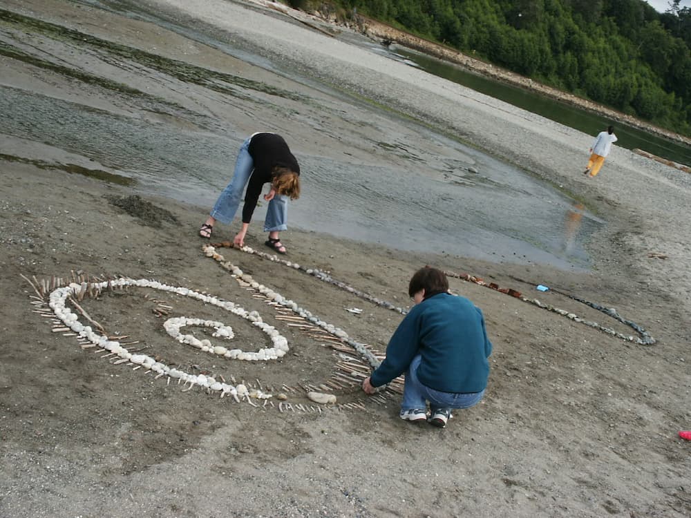 Two people collaborating to build a stone and driftwood spiral on the beach