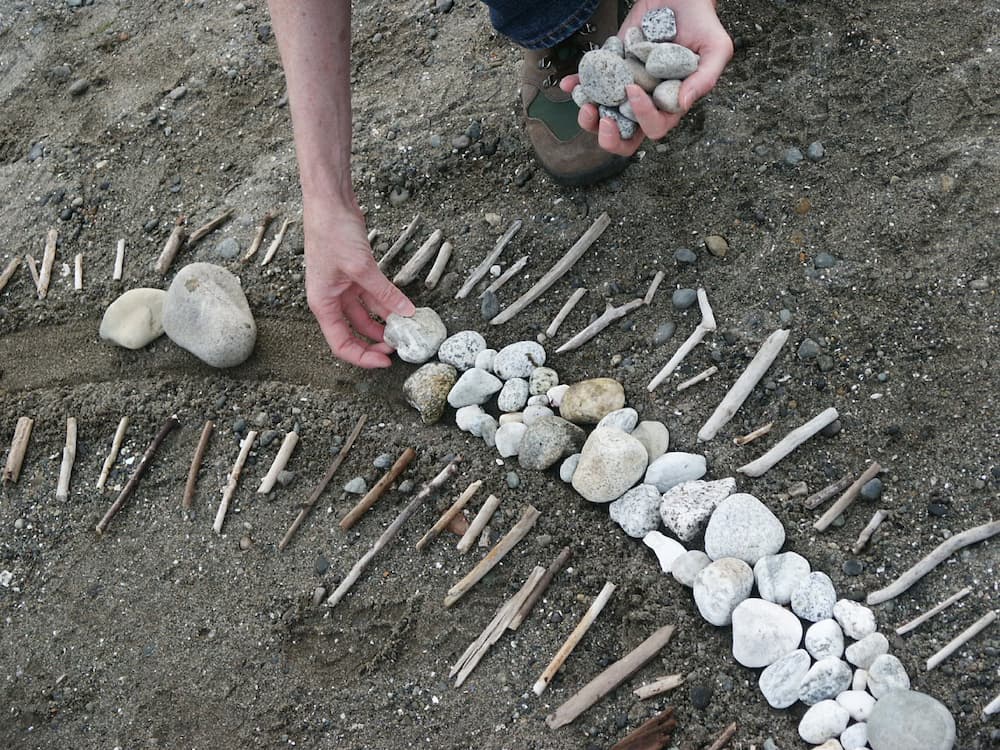 Hands placing stones into a spiral on the beach at Puget Sound